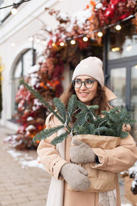 A stylish young woman wearing a hat with branches of nobilis in a  bag walks around the christmas