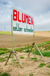 Signboard on field against cloudy sky