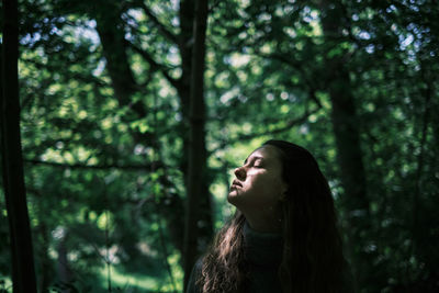 Side view of young woman standing in forest