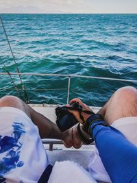 Low section of men in boat on sea against sky