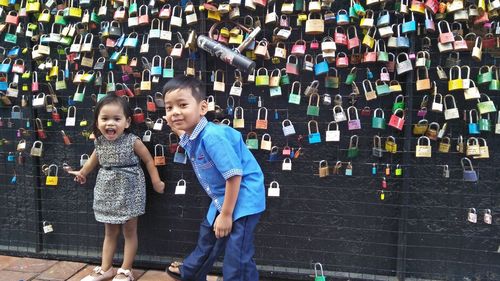 Portrait of siblings standing by colorful love locks hanging on metal grate