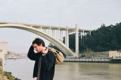 Man standing on bridge over river in city against clear sky