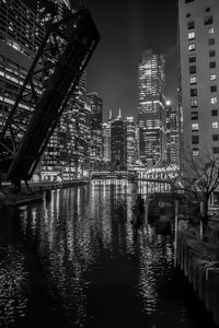 Illuminated buildings by river against sky in city at night