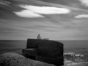 Rear view of man on rock formation by sea against sky