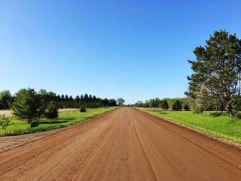 Road amidst trees on field against clear sky