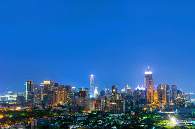 Illuminated buildings in city against blue sky