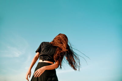 Low angle view of woman tossing hair against clear sky