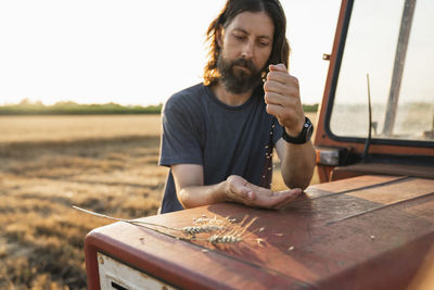 Mature man holding grain standing by tractor at farm