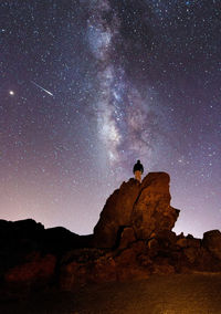 Low angle view of man on rock against star field