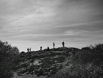 Silhouette people standing on rocks against cloudy sky