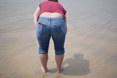 Rear view of woman bending while standing on shore at beach