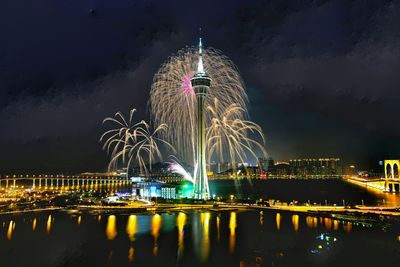 Illuminated ferris wheel in city against sky at night