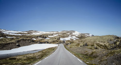 Road amidst mountains against clear blue sky