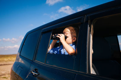 Portrait of boy in car against sky