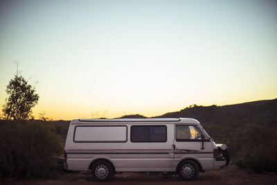 Van parked in field against sky during sunset