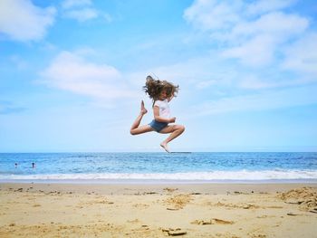 Woman jumping on beach against sky