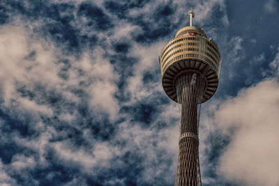 Low angle view of communications tower against cloudy sky