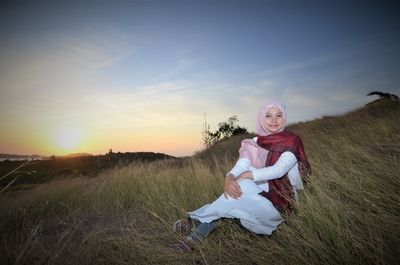 Portrait of woman in headscarf sitting on field against sky during sunset