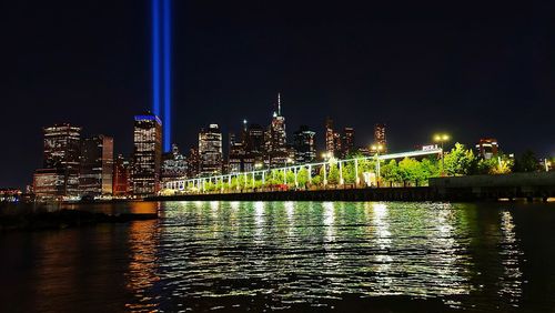 Illuminated buildings by river against sky at night