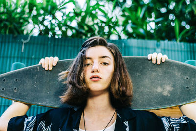 Teenage girl with longboard on her back with hawaiian shirt