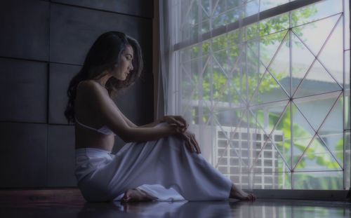 Side view of thoughtful young woman sitting on floor at home