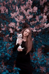 Portrait of woman carrying dog while standing against plants