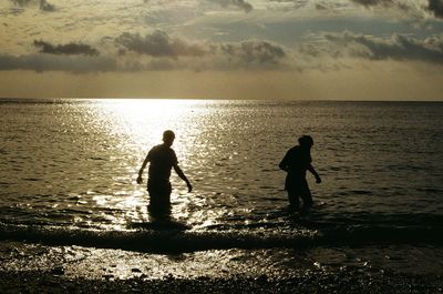 Two people walking into the sea at dusk 