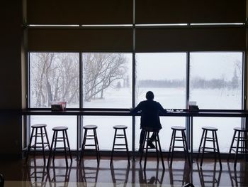 Rear view of man sitting on stool in restaurant during winter