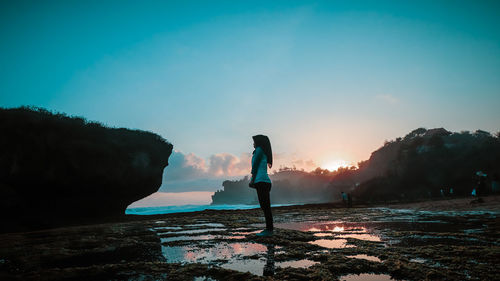 Silhouette woman standing on beach against sky during sunset