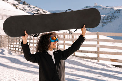 African american woman with goggles and a snowboard on a snowy mountain during winter