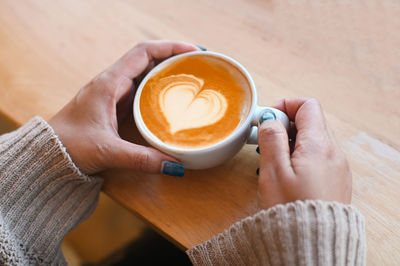 Cropped hands of woman holding coffee on table