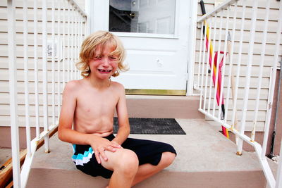 Boy crying in pain while sitting on steps outside house