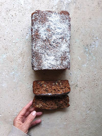 Hand holding slice of date and walnut loaf cake on stone table