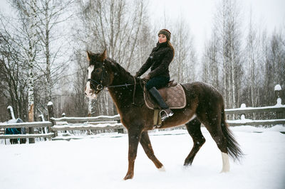 Beautiful woman riding horse on snow covered field