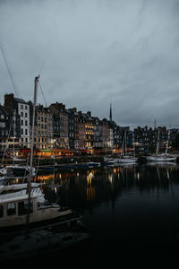 Sailboats moored in city against sky at dusk