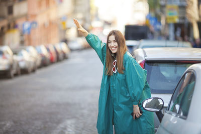 Portrait of smiling woman gesturing while standing by cars on street in city