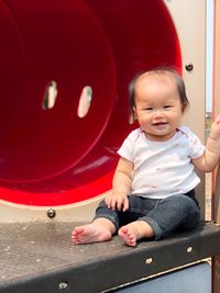 Full length of smiling cute girl sitting on equipment in playground