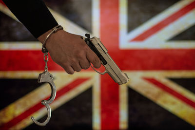 Cropped hand with handcuffs holding gun against british flag