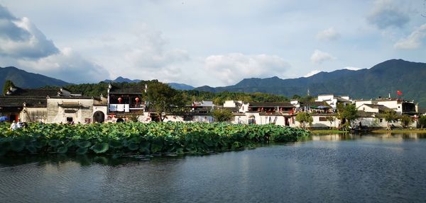 Houses by lake and buildings against sky