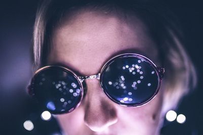 Close-up of young woman wearing sunglasses in illuminated room