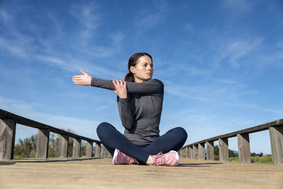 Sporty woman sitting crossed legged doing a shoulder stretch warm up exercise.