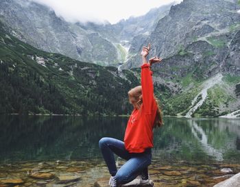 Woman kneeling at lakeshore against mountains