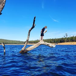 Side view of man in sea against blue sky