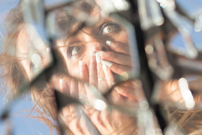 Close-up of mid adult woman with hands covering mouth reflecting on broken glass