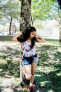 Portrait of young woman standing on tree trunk