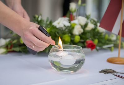 Cropped hand of woman lighting tea light in container on table