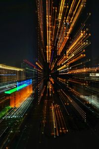 Light trails on illuminated city against sky at night
