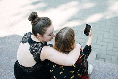 Young women girlfriends lgbt couple photographing with mobile phone while standing outdoors