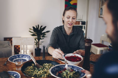 Happy woman serving cherry tomatoes to man in plate at home