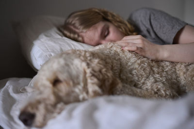 Crying young woman hugging dog in bed